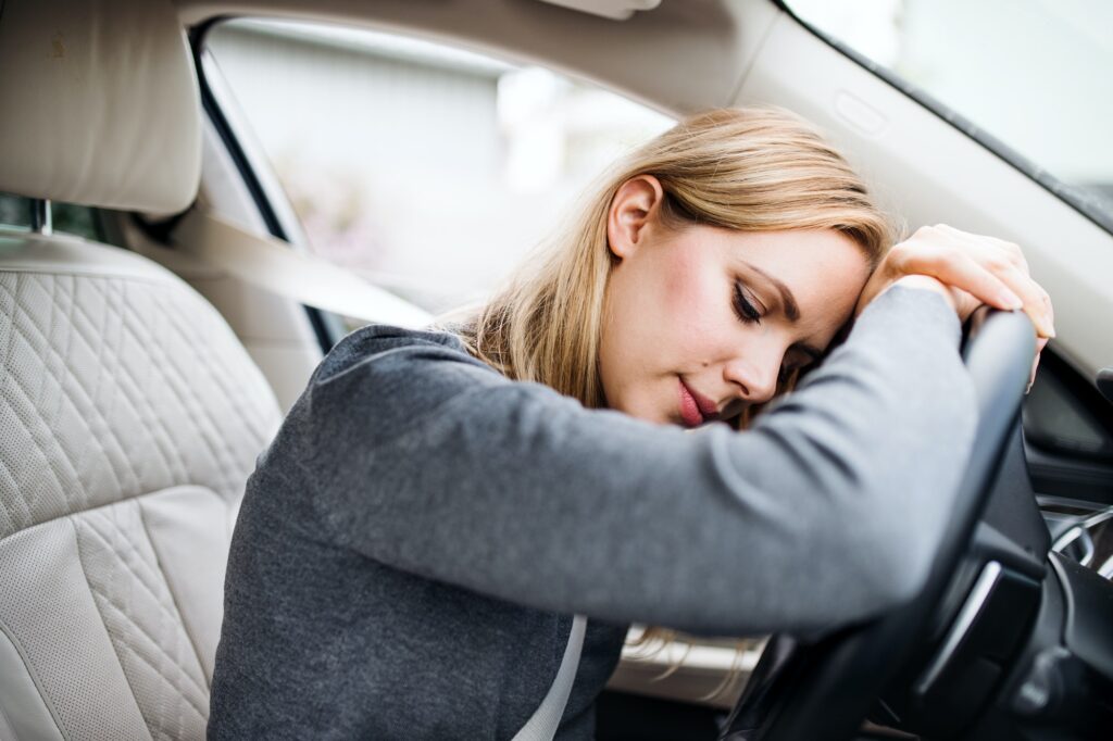 Tired young woman driver sitting in car, head resting on steering wheel